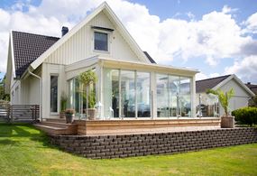 Vitt uterum i modern stil med glastak, anslutet mot hus med vit träpanel.